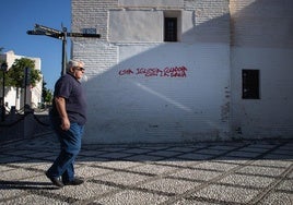 A resident walks past the façade of the church of San Nicolás, where a vandal has spray-painted red graffiti.