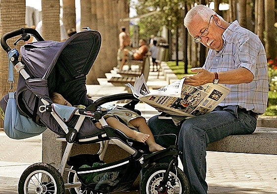 A citizen reads a regional newspaper while taking care of his grandson in an Andalusian park.