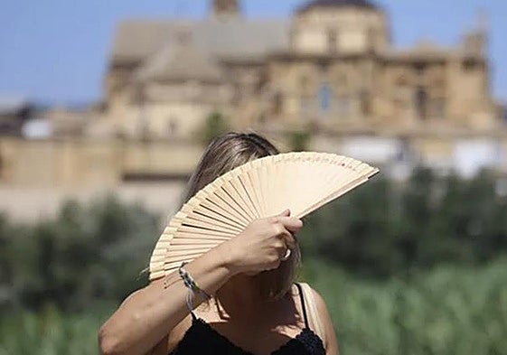 A woman fans herself as she crosses the Roman bridge in Cordoba on a hot day.