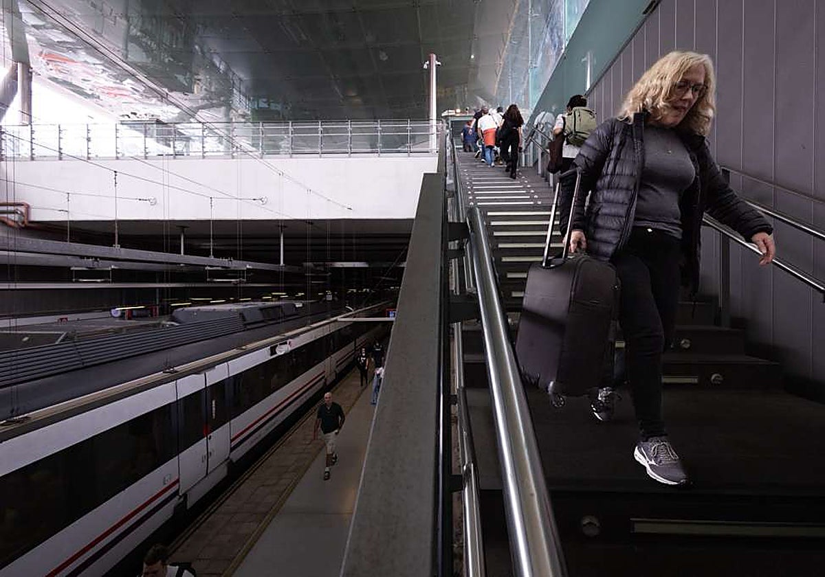 A passenger struggles down the steps to the station platform, carrying her suitcase in hand.