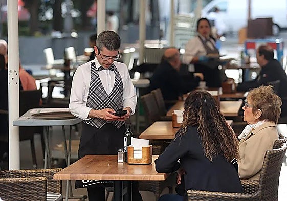 A waiter taking payment from two customers at a restaurant in Spain.