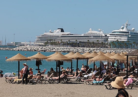 Archive photo of sunbathers on the beach in Malaga with several cruise ships in the background.