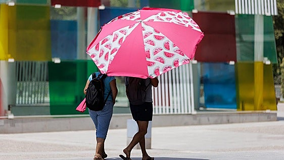 Two people are seeking shelter from the heat under a beach parasol at Muelle Uno in Malaga.