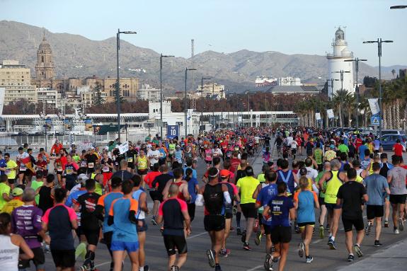 Runners cross the Malaga port, with the cathedral and lighthouse in the background.