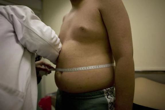 A doctor meausures the waist of a young male suffering from excess weight.
