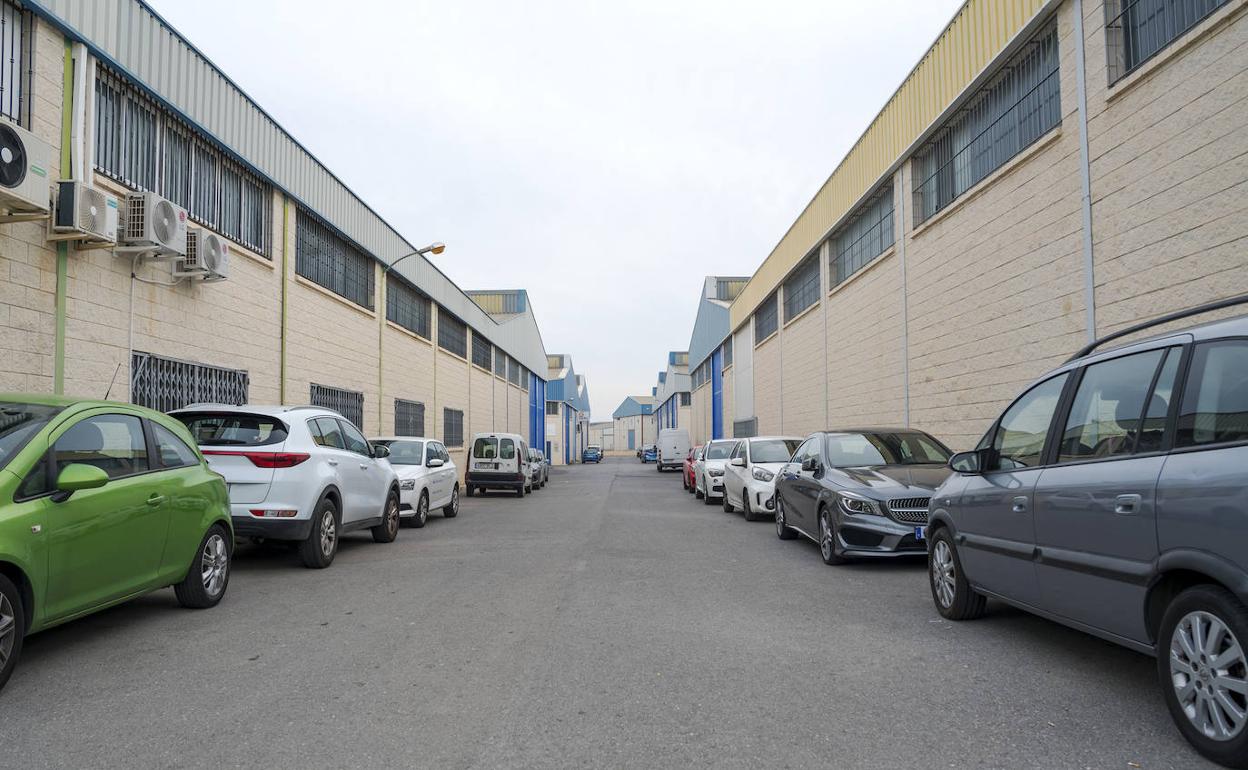 Coches aparcados en una calle que separa dos naves industriales