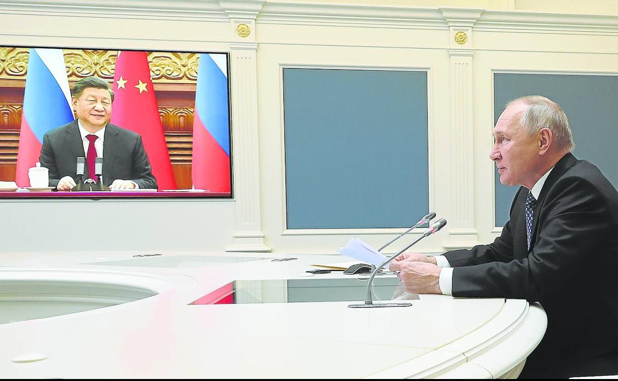 Putin, sentado en una sala del Kremlin, mantiene la videoconferencia con Xi Jinping.