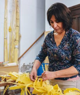 Imagen secundaria 2 - Paqui Serrano trenzando palma blanca en el taller familiar. 