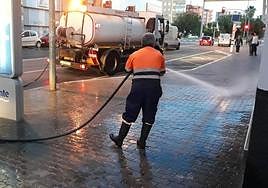 Un operario de limpieza baldea las aceras con el camión cisterna.