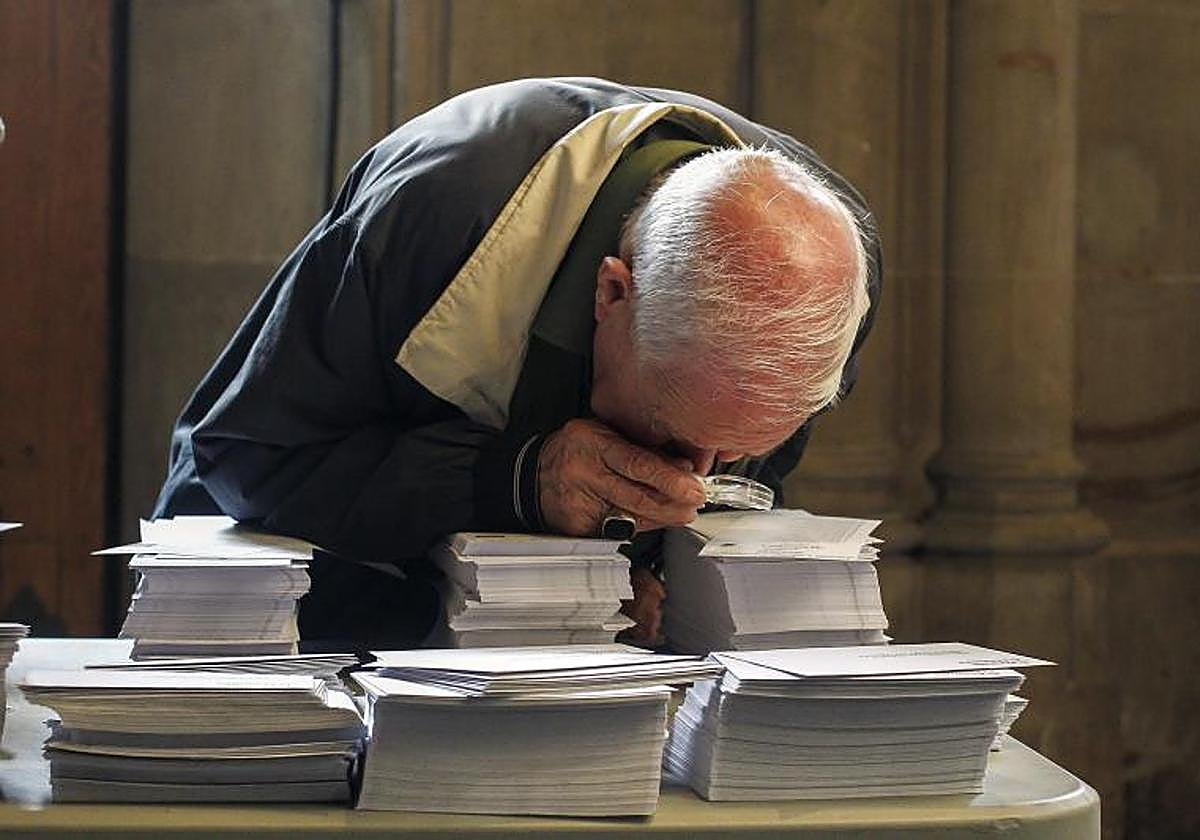 Una persoma observa con una lupa las papeletas de los diferentes partidos que concurren a las elecciones.