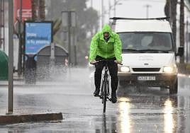 Un hombre en bicicleta se resguarda con un chubasquero bajo la lluvia