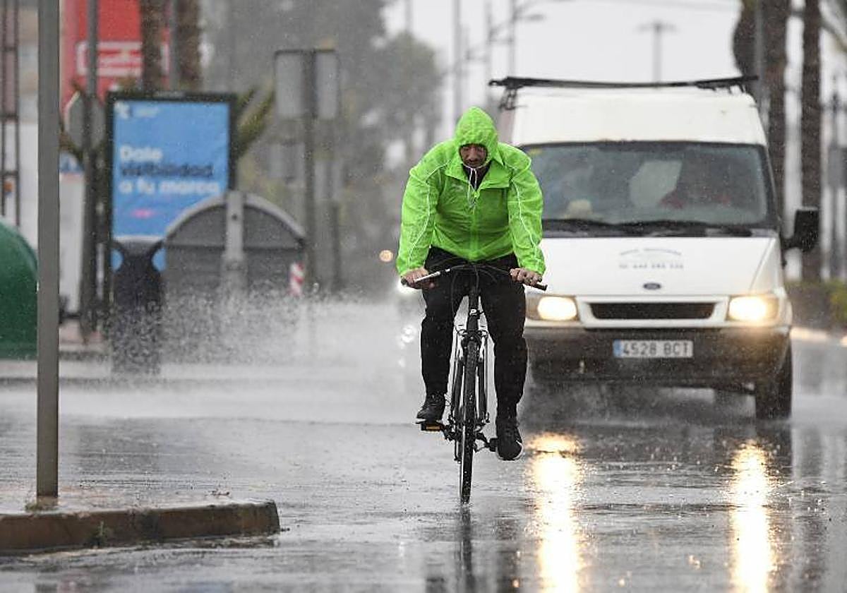 Un hombre en bicicleta se resguarda con un chubasquero bajo la lluvia