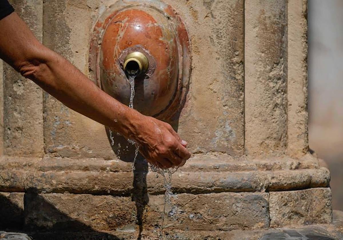 Un hombre se refresca la muñeca en una fuente.