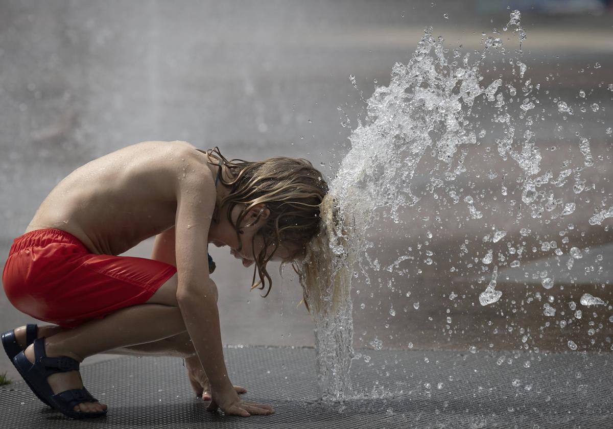 Un niño se refresca en una fuente pública.