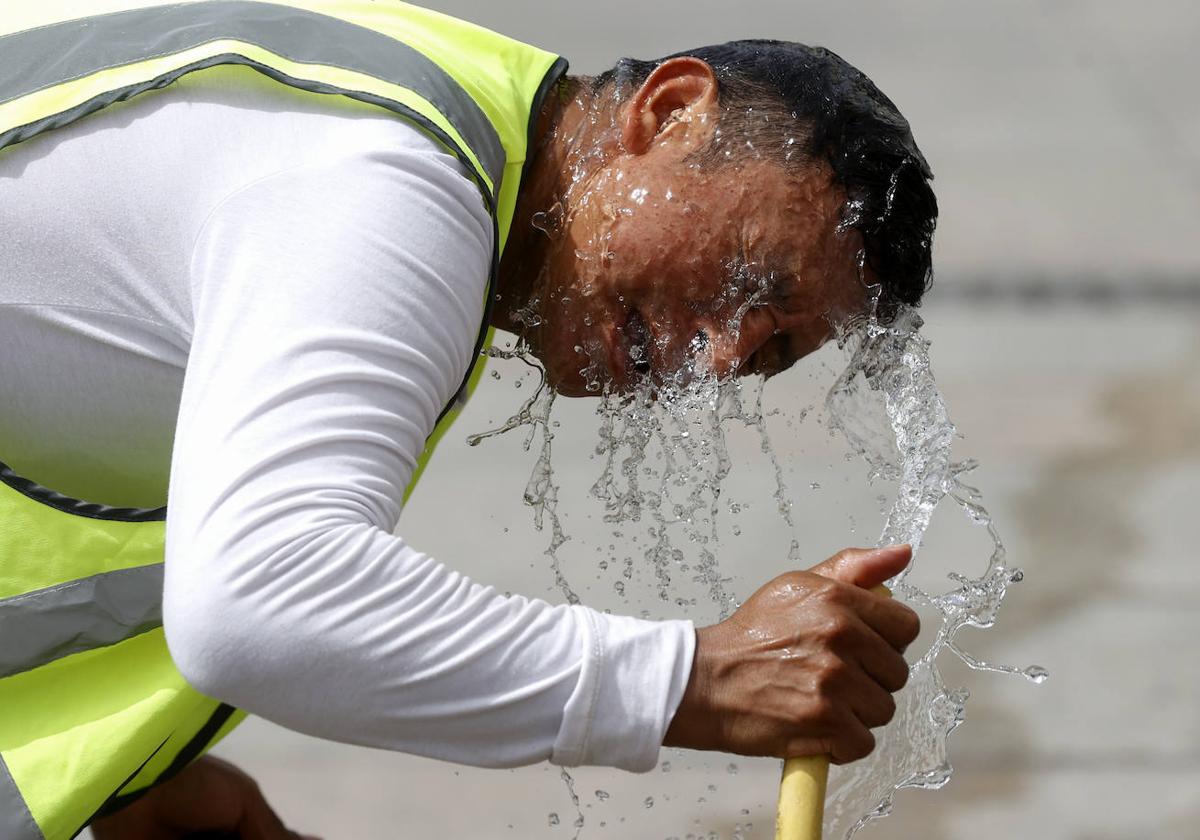 Un trabajador se refresca con una manguera en la calle.