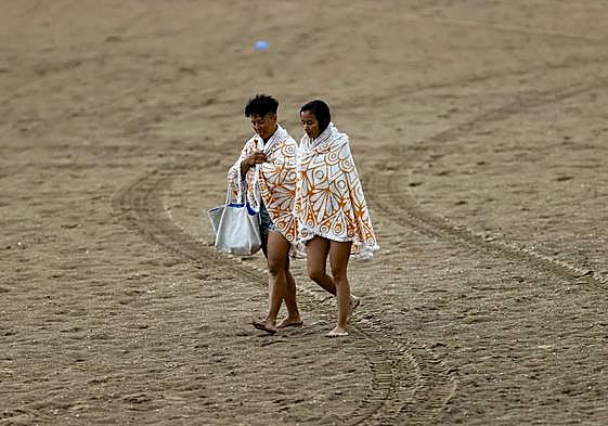 Bañistas huyen de la playa, cubiertas, tras el temporal de lluvia.