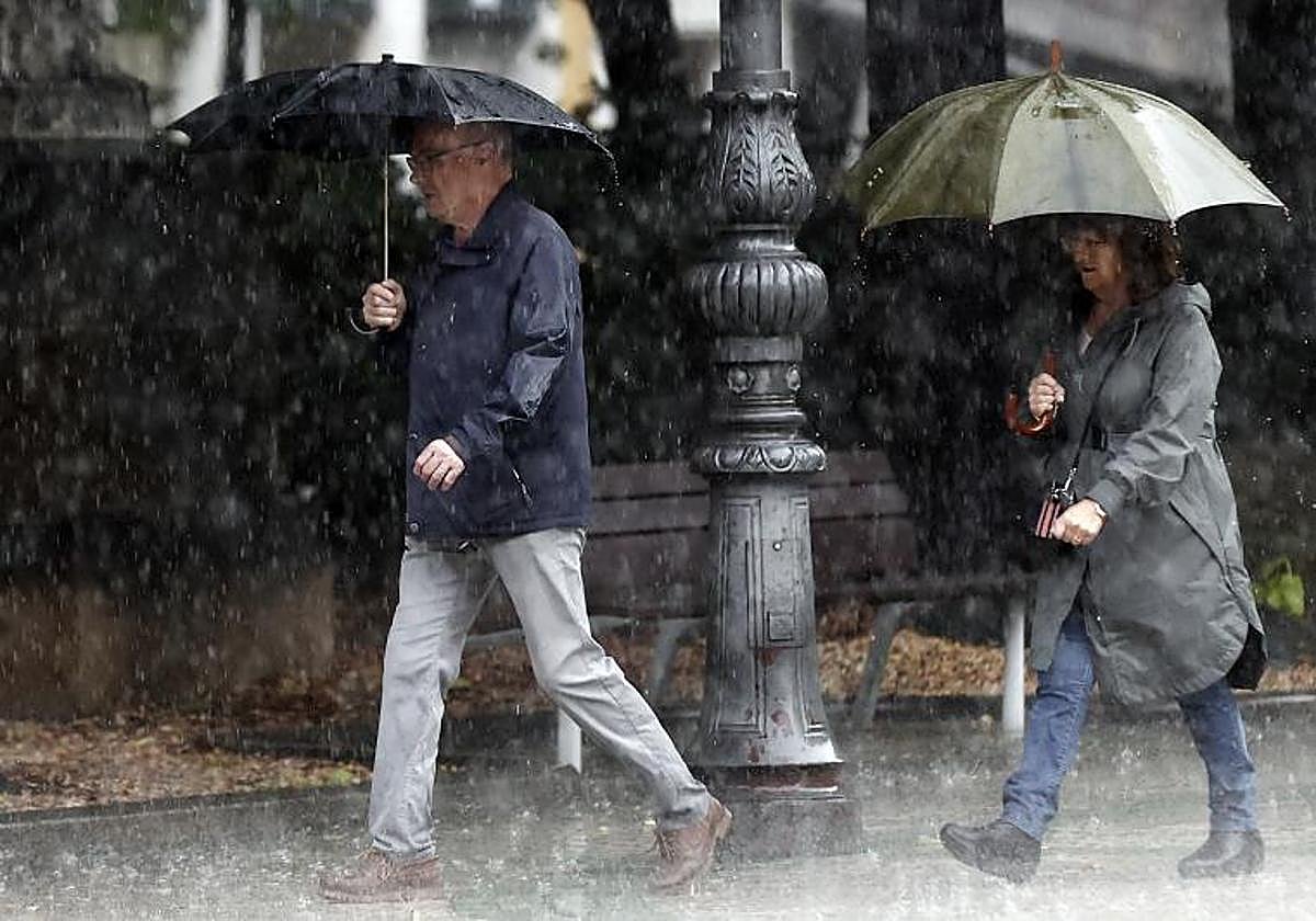 Dos viandantes pasean bajo la lluvia.