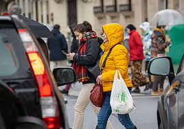 Una mujer cruza un paso de cebra con un abrigo.