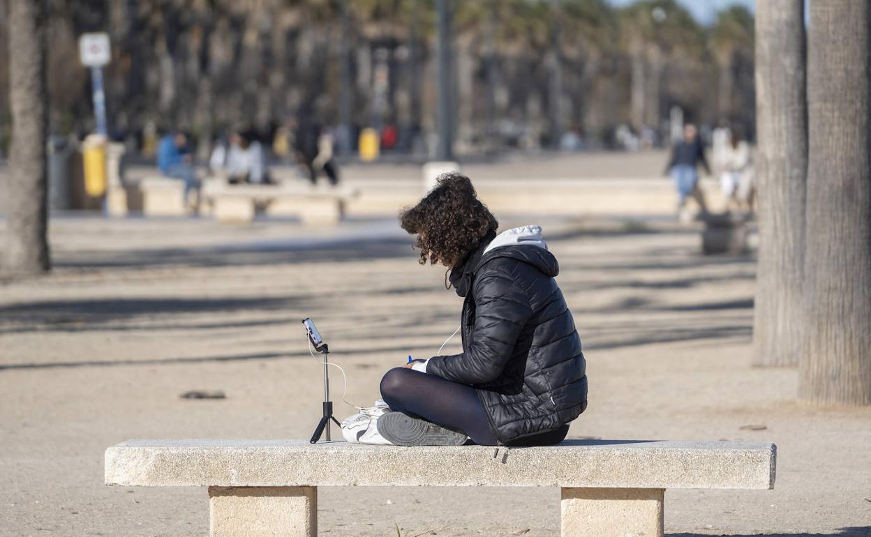 Una mujer se sienta en un banco al sol y abrigada por el frío