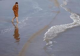 Un hombre con abrigo entra descalzo en el mar.