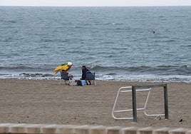 Varias personas desafían a la lluvia en una playa de Alicante.