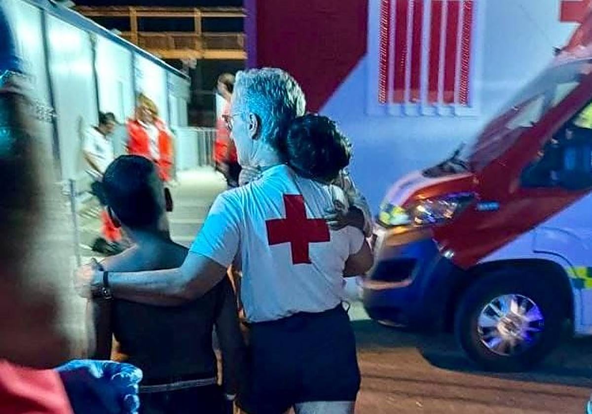 Un voluntario de Cruz Roja acompaña a dos menores llegados a puerto.