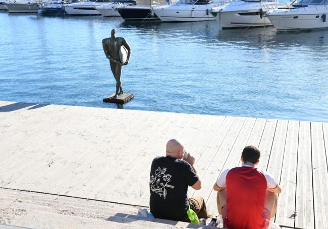 Dos alicantinos descansan en el Puerto, frente a la escultura de Ícaro sin agua en los pies.