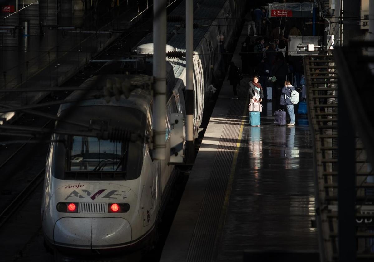 Several people next to an AVE train stationed at Atocha-Almudena Grandes station.