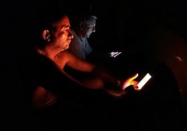 Dos hombres consultan sus móviles de noche.