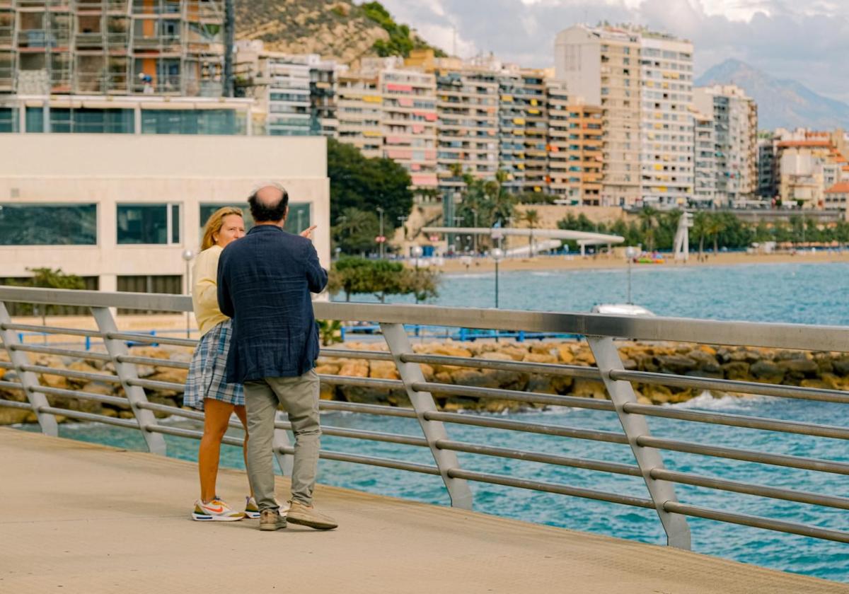 A couple of tourists on the port walkway, behind the Spa Porta Maris, gaze at Postiguet Beach.