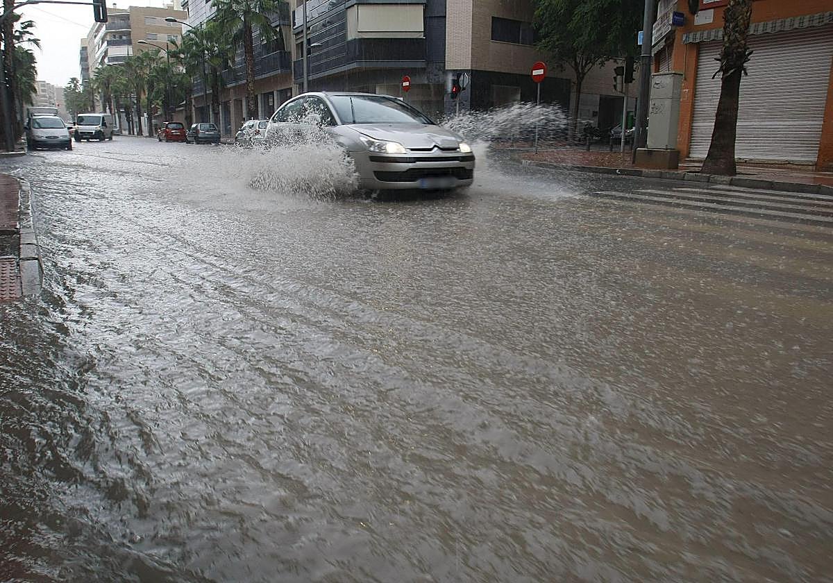 Coche circulando por una calle llena de agua de las lluvias en San Vicente del Raspeig.