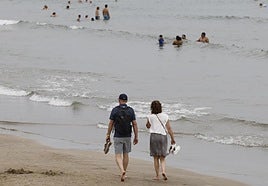 Una pareja pasea por el borde de la playa.