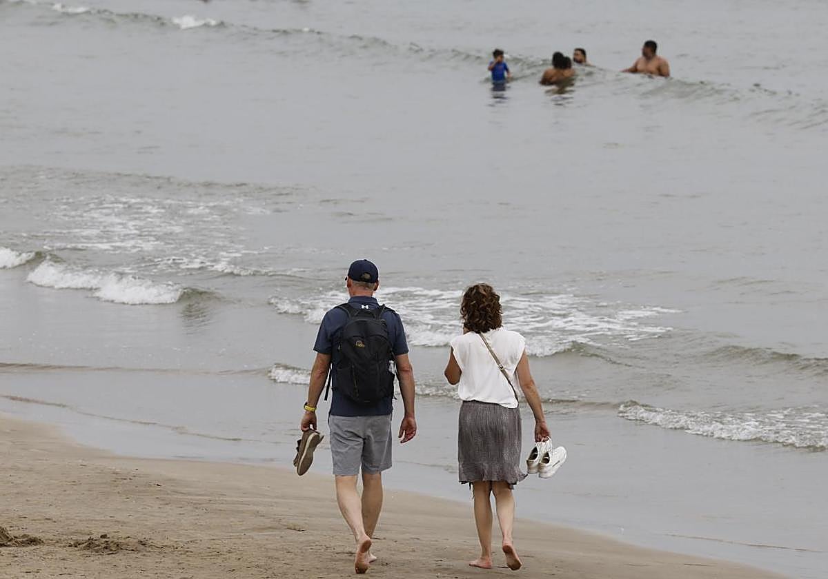 Una pareja pasea por el borde de la playa.