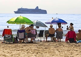 Turistas en la playa del Postiguet ven pasar un crucero.