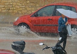 Una viandante se intenta refugiar de la tromba de agua bajo un paraguas en Alicante.