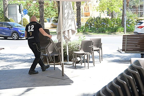 Un camarero recoge sillas en una terraza.