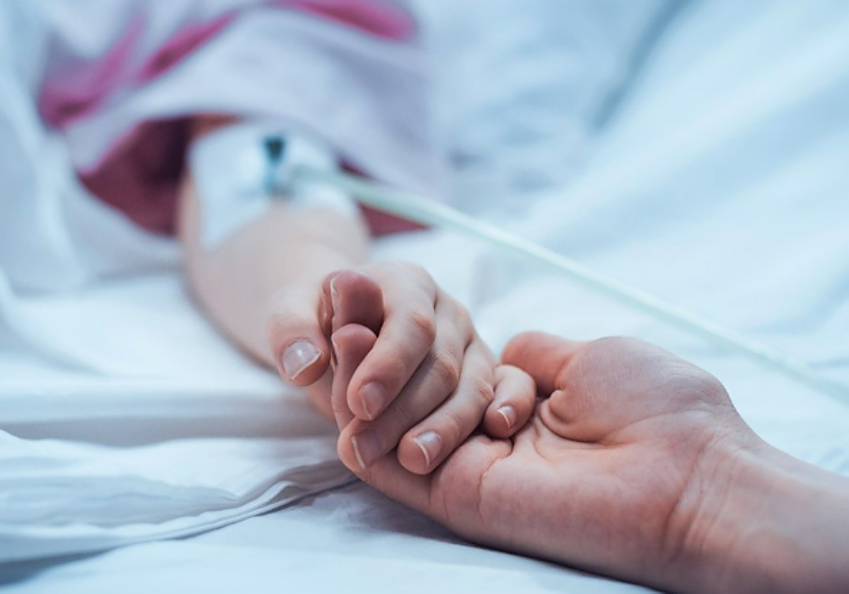 An adult holds the hand of a hospitalized child.