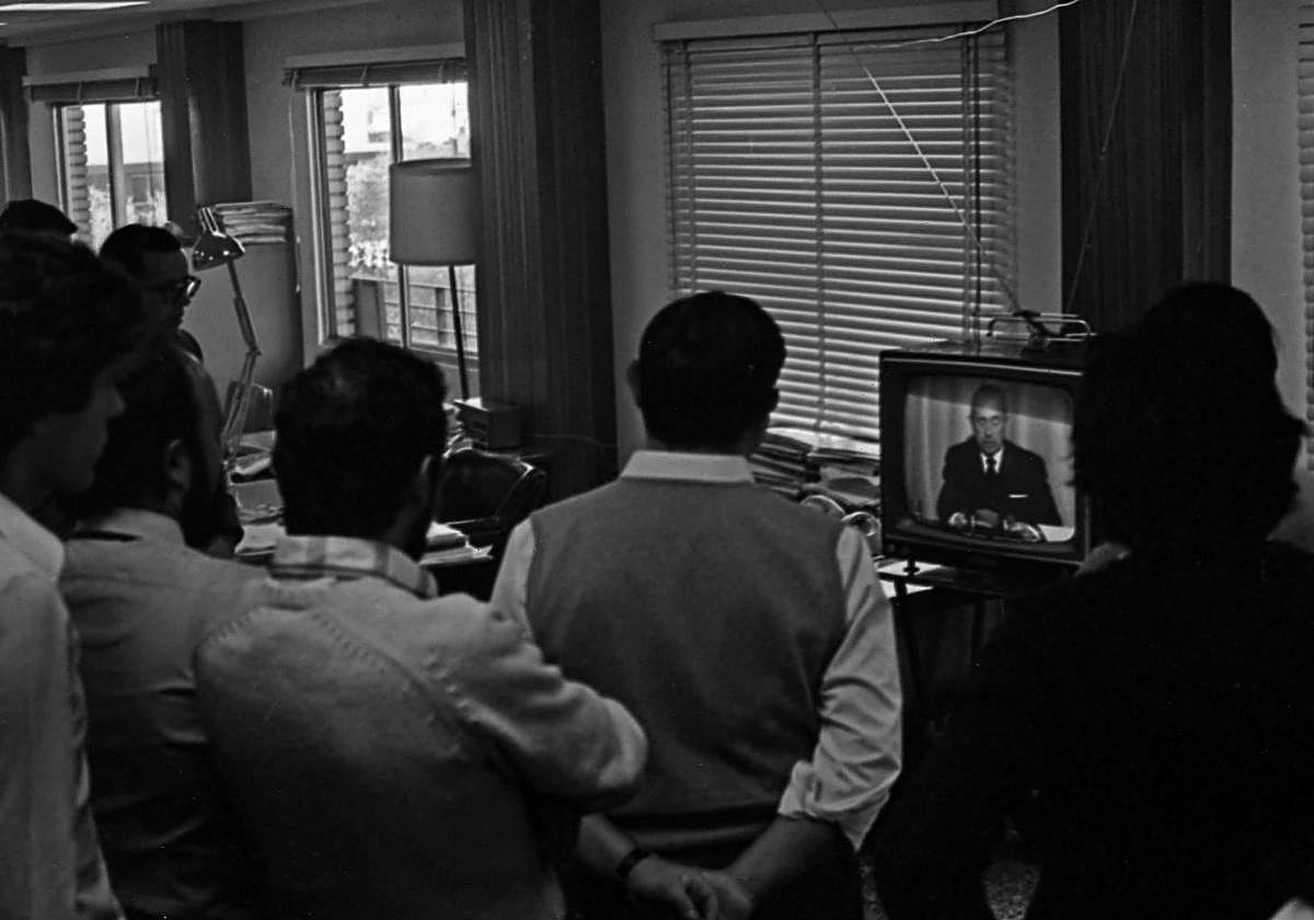 Un grupo de personas se juntan delante de la televisión para oír el anuncio de la muerte de Francisco Franco.